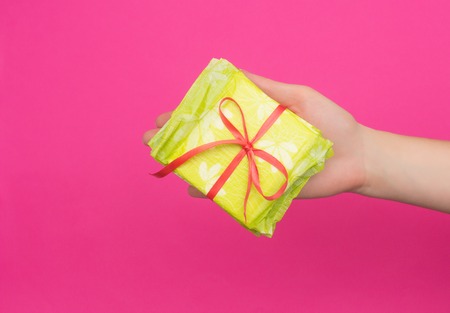 Female hand holding a stack of sanitary pads tied with a red ribbon in her hand, pink background, copy space, critical days, intimateの写真素材