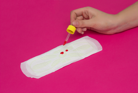 A girl is dripping drops of blood on the female gasket for menstruation in girls, the concept of critical days, pink background, close-up, copy space, monthly, cycleの写真素材