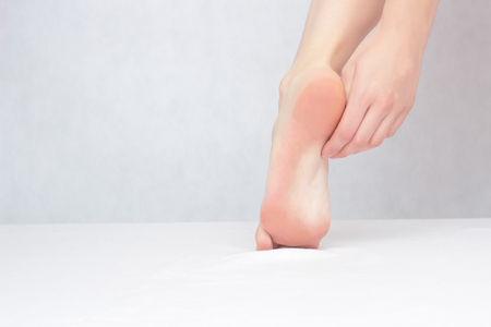 Girl touches his foot with his foot and heel on a white background, close-up, copy space, onychomycosis, fungusの写真素材