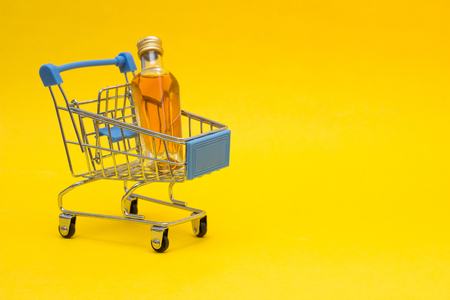 Small bottle with alcohol in a shopping basket, close-up, copy space, orange background, purchasesの写真素材