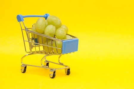 Grapes in a shopping trolley on a yellow background, close-up, copy spaceの写真素材