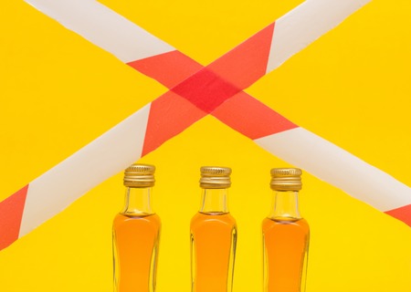 Small bottles of alcohol on a yellow background and red tape concept of sanction, day of sobriety, a ban on alcohol, productsの写真素材