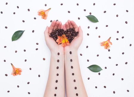 Female hands with coffee beans and hibiscus flowers on a white background, background design art, cosmeticの写真素材