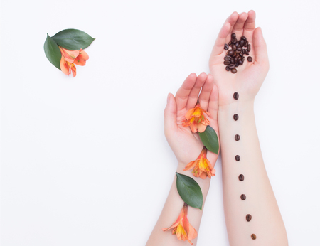 Female hands with coffee grains and hibiscus flowers and petals on a white background, fashionable art, copy space, handfulの写真素材