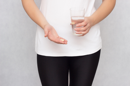 The girl holds a glass of water and an anesthetic pill in her hand during menstruation and PMS, pain, anaesthetiseの写真素材
