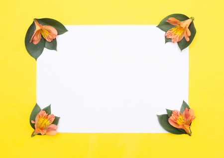 Blank white paper on a yellow background with petals and orange hibiscus flowers, greeting card mockupの写真素材