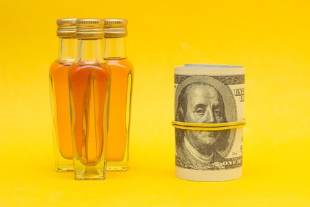 Small bottles with alcohol on a yellow background and money dollars, the proceeds from the sale of alcohol, close-up, cognacの写真素材