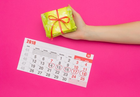 Calendar with marked days of menstruation in a girl, female hand with a stack of sanitary pads, pink background, background, protectiveの写真素材