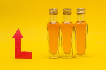 Small bottles of alcohol on a yellow background and a red arrow concept of raising the price of alcohol, close-upの写真素材