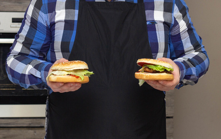 Fat man in a black apron holds two hamburger, close-up, copy space, junk foodの写真素材