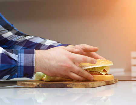 A man holds in the hands of the kitchen fatty juicy hamburgers, junk food, close-up