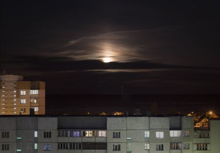 Creepy moon in the night sky against the background of urban houses and buildings, the influence of the moon on humansの写真素材
