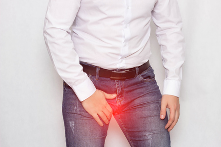 A man on a white background in a white shirt holding on to his groin he has pain and varicocele of the spermatic cord, a problem, varicose veins, spermatogenesisの写真素材