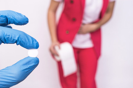 Doctor holding a pill in her hand against the background of a girl with toilet paper, concept pills...