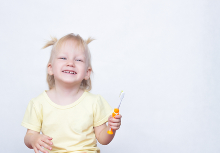 Little girl 2 years old with pigtails in her hair laughs and brushes her teeth on a white background, copy space, toothpasteの写真素材