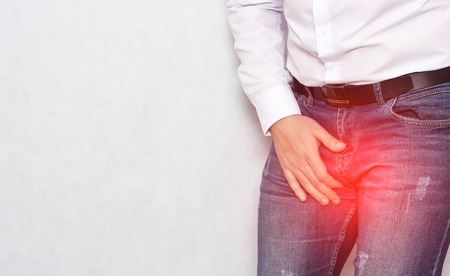 A man in a white shirt holding his groin with an infection and prostatitis, urology, copy space, varicocele, spermatogenesisの写真素材