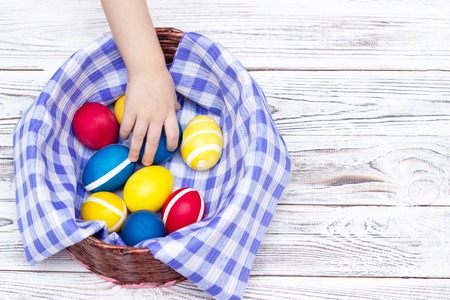 children's hand takes from the basket colorful Easter eggs that lie on a motley fabric and on a...