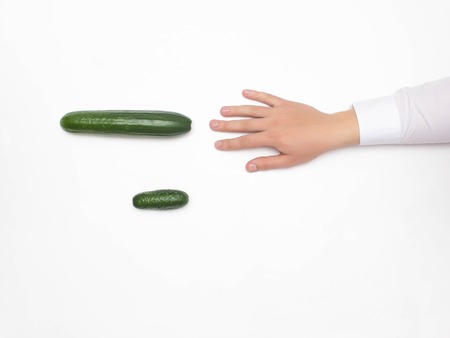 Male hand on a white background reaching for a big cucumber, the concept of increasing the male member using different techniques, medical, copy spaceの写真素材