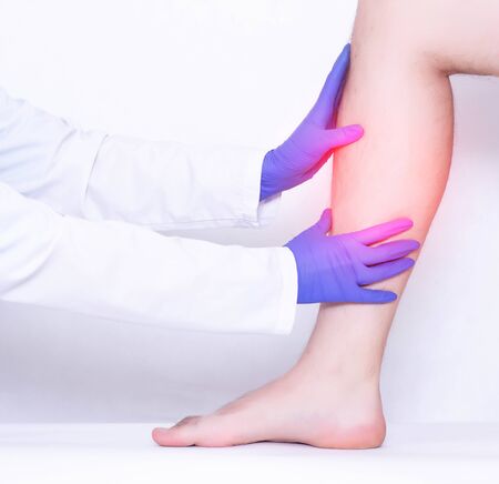 The surgeon conducts a medical examination of the damaged calf ligaments on the leg of a man,...