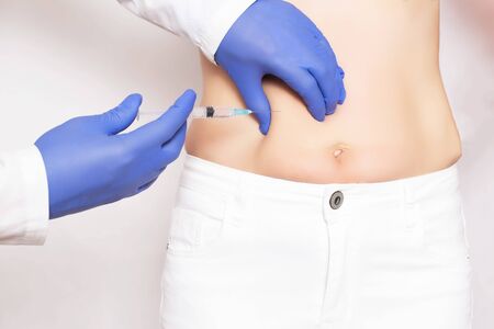Doctor cosmetologist makes  injections and rejuvenation in the stomach of a girl. Smoothing wrinkles and wrinkles on the abdomen with the help of hyaluronic acid rejuvenation injectionsの写真素材