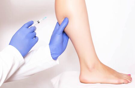 Doctor cosmetologist makes rejuvenation beauty injection to the calf muscle on the leg of the girl. Rejuvenation with injections of Hilauri acidの写真素材