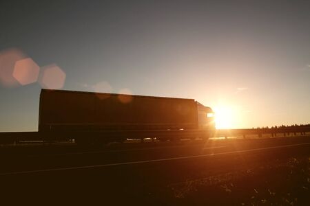 Modern wagon truck transports cargo against the backdrop of a sunset. The concept of truck drivers in the field of freight and logistics, copy spaceの写真素材