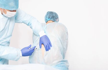 A male anesthesiologist performs a surgical procedure that introduces epidural anesthesia into the back of a girl during childbirth, medic, copy space, epidural anesthesiaの写真素材