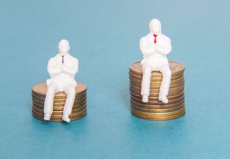 Two toy people are sitting on money dollars cents concept of earnings of a worker and a boss. Salary...