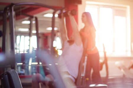 Girl personal trainer teaches a man fitness exercises in the gym, sunset, background, blurred,...
