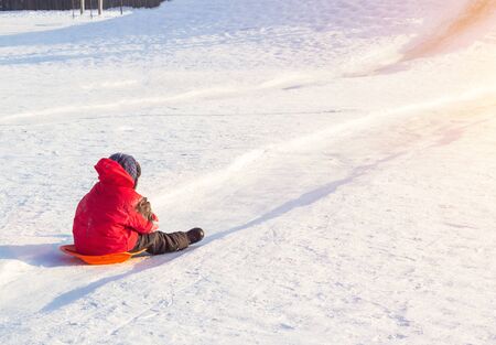 Little boy in bright red clothes rolls down a hill in frosty winter weather, copy space, outdoorの写真素材