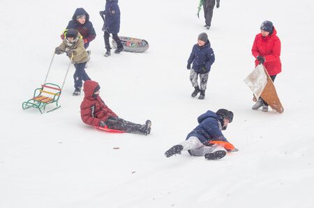 A lot of people children and adults ride a sled in the winter in the snow, gladness. BOBRUISK, BELARUS - 03.01.19のeditorial素材