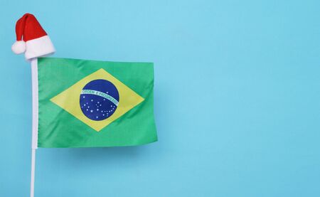 Flag of Brazil with little santa claus hat on blue background. New Year winter holiday concept, copy...