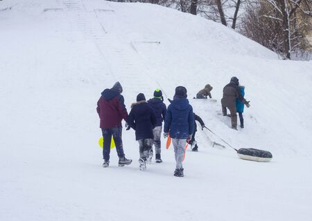 A lot of people children and adults ride a sled in the winter in the snow, gladness. BOBRUISK, BELARUS - 03.01.19のeditorial素材