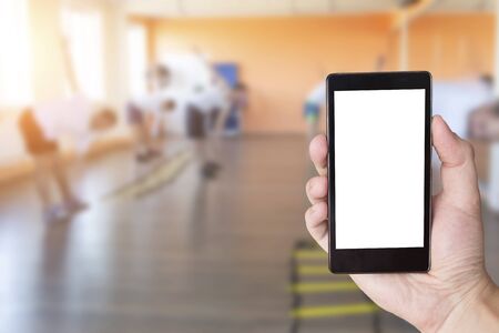 Hand with mobile phone in the background of people engaged in a fitness center. Gym and fitness phone app concept, copy space, smartphone, textの写真素材