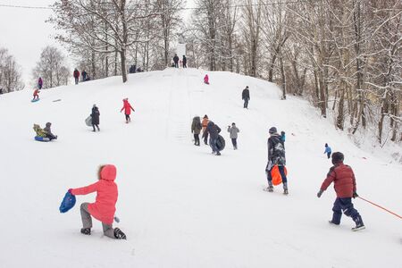 A lot of people children and adults ride a sled in the winter in the snow, gladness. BOBRUISK, BELARUS - 03.01.19のeditorial素材