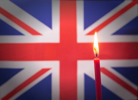 Burning candle on the background of the flag of United Kingdom. The concept of mourning and sorrow in the countryの写真素材