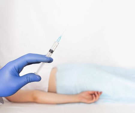 The doctor holds a syringe in a glove against the background of a patient with varicose veins and hemorrhoids. Sclerotherapy treatment concept, copy space, spider veinsの写真素材