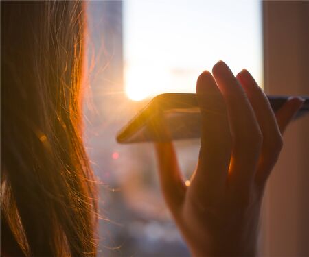 Girl holds a smartphone in her hand on a background of sunny sunset. Concept phone application for people with disabilities, disabled, blindの写真素材
