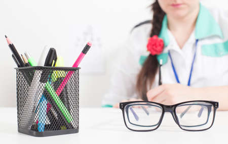 Glasses for the eyes in the foreground, in the background the doctor an ophthalmologist writes out a prescription in the doctor s office, conjunctivitisの写真素材