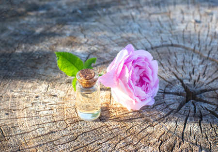 Bottle of perfume with perfume from a rose on a wooden background. The concept of delicious aroma of flowers, aromatherapy