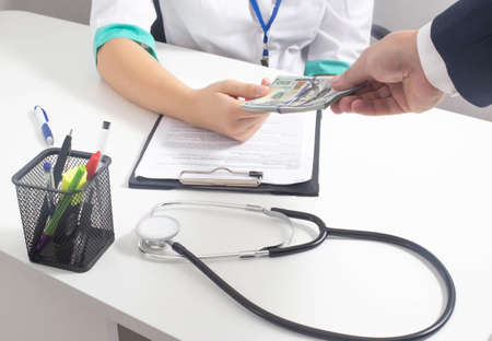 The man hands the money dollars to the doctor. Concept of payment for paid services in medicine, healthcare and money, paymentの写真素材
