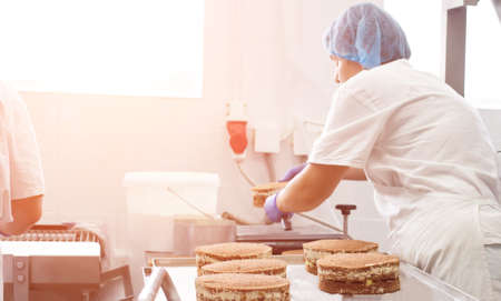 Making sponge cakes with cream at a confectionery factory. Cook decorates cake with cream, sweet...