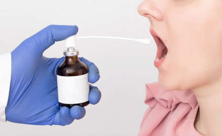 Doctor sprays antimicrobial and anti-inflammatory spray into a girl's sore throat, close-up. Concept...
