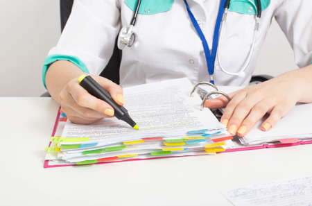 The woman doctor highlights the necessary information in the papers with a felt-tip pen. Patient...