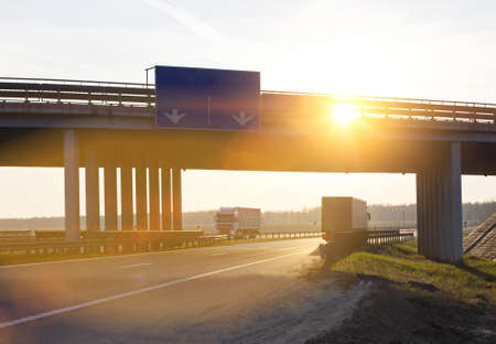 Trucks with semi-trailers move along the highway against the backdrop of a sunny sunset. Automobile...