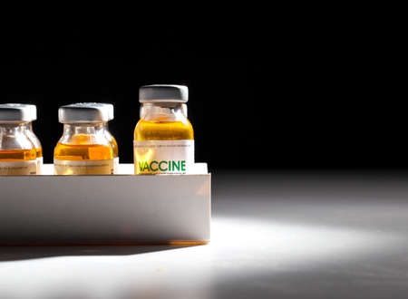 Vials with coronavirus vaccine in packaging on a black background and illuminated by a beam of...