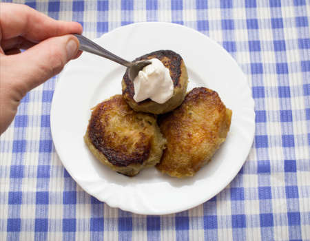 A plate with a Belarusian dish potato pancakes with meat filling and sour cream. Blue checkered...