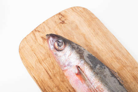 Red-eyed sea fish on a wooden kitchen board on a white background, isolate. Close-up, macro, studio...