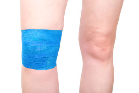 Blue elastic bandage on the knee joint to fix the sore kneecap, white background, isolate.の写真素材