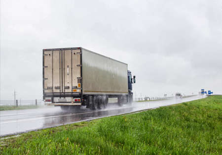 A trucker on a truck with a semitrailer transports cargo in poor visibility on the road, rain. Highway traffic in bad weather. Copy space for text, dangerの写真素材